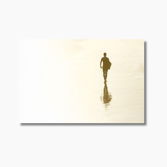 Surfer walking on wet sand with reflection at sunset, capturing the golden hues of the sun on the beach at Snapper Rocks.