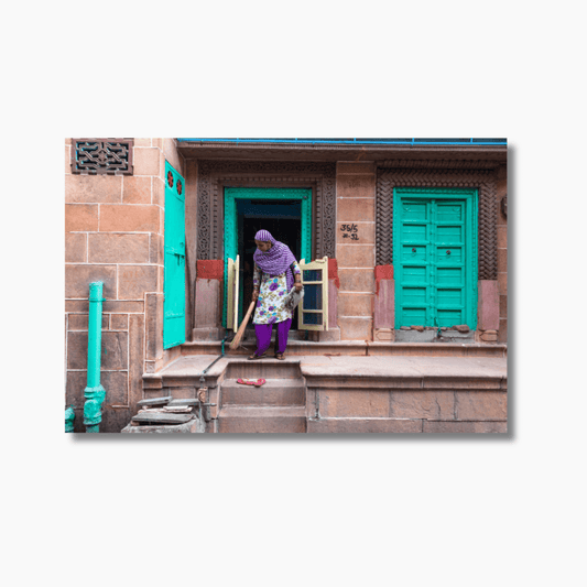 Indian woman sweeping outside her front door in the blue streets of Jodhpur — limited edition cultural street photography print.