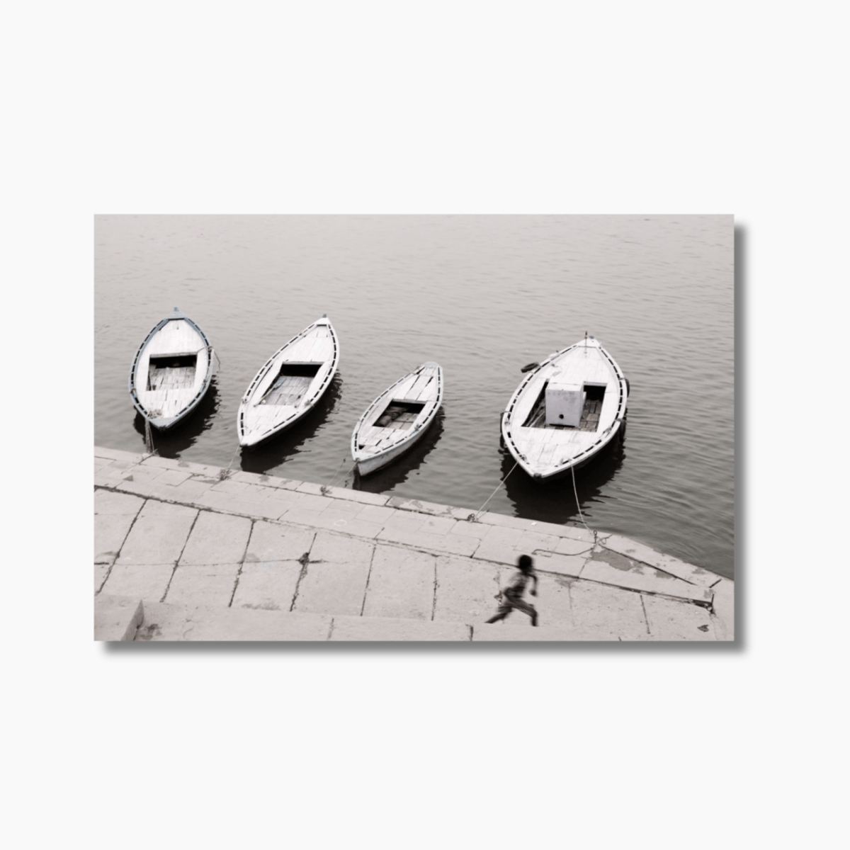 Boy running along the Ganges River in Varanasi, India, with wooden boats in the background — limited edition cultural photography wall art print.