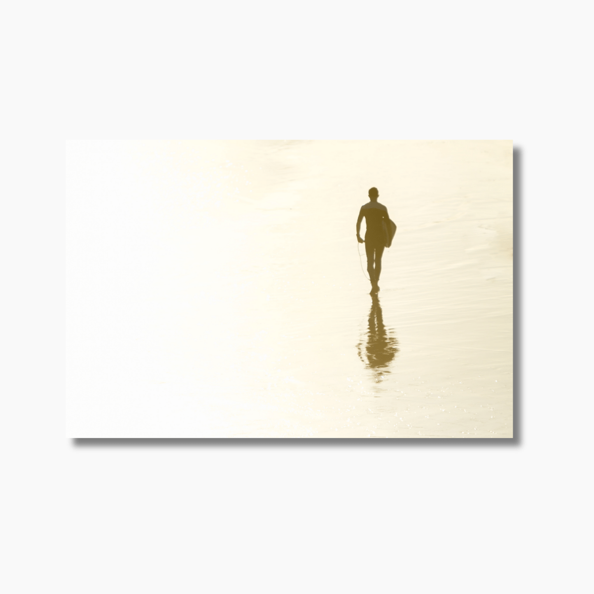 Surfer walking on wet sand with reflection at sunset, capturing the golden hues of the sun on the beach at Snapper Rocks.